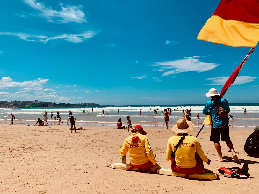 life guards are putting up a red and yellow flag at the beach on a bright, sunny day