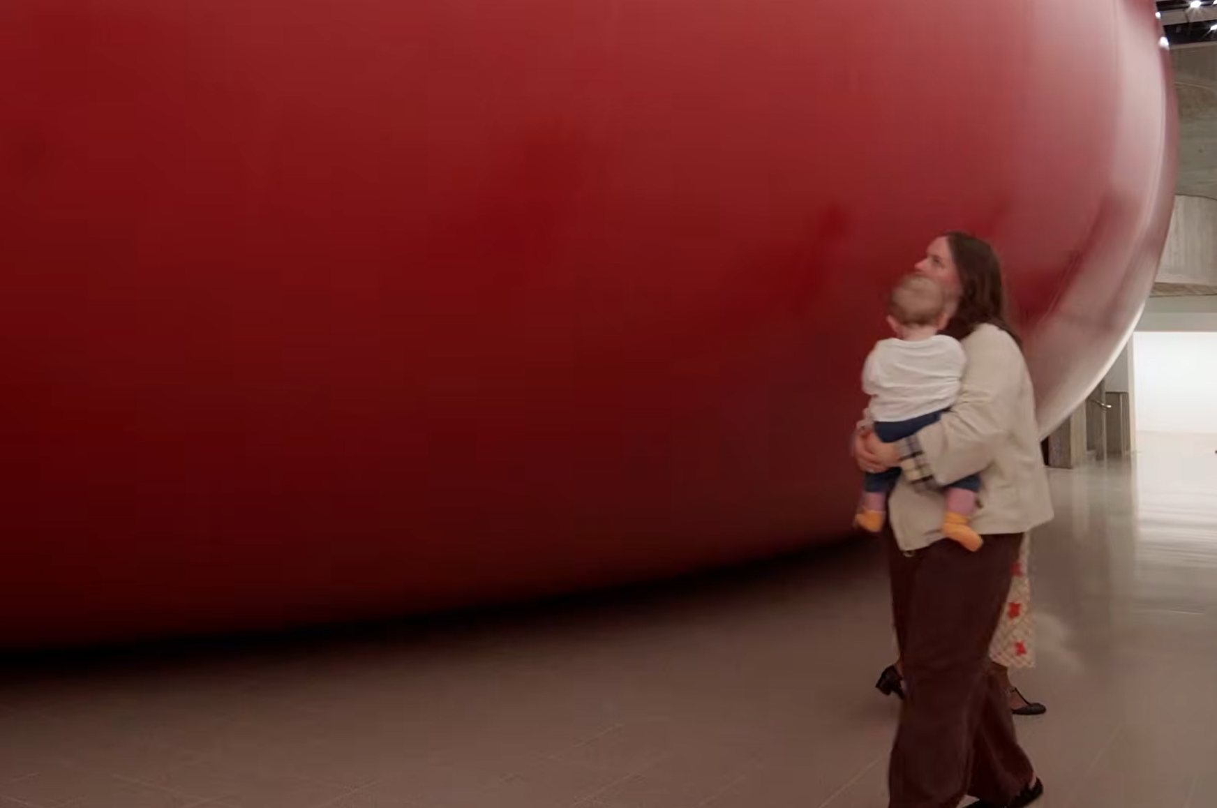 An eye-level view from the gallery floor looking directly at a massive, inflated dark-red membrane blocking the usual entrance to the gallery.