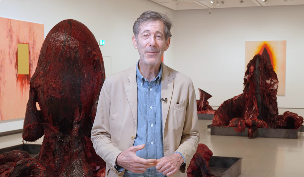 An eye-level view of huge simulated red, fleshy remains lying on industrial metal trays, rising in some parts to a height taller than a person standing.