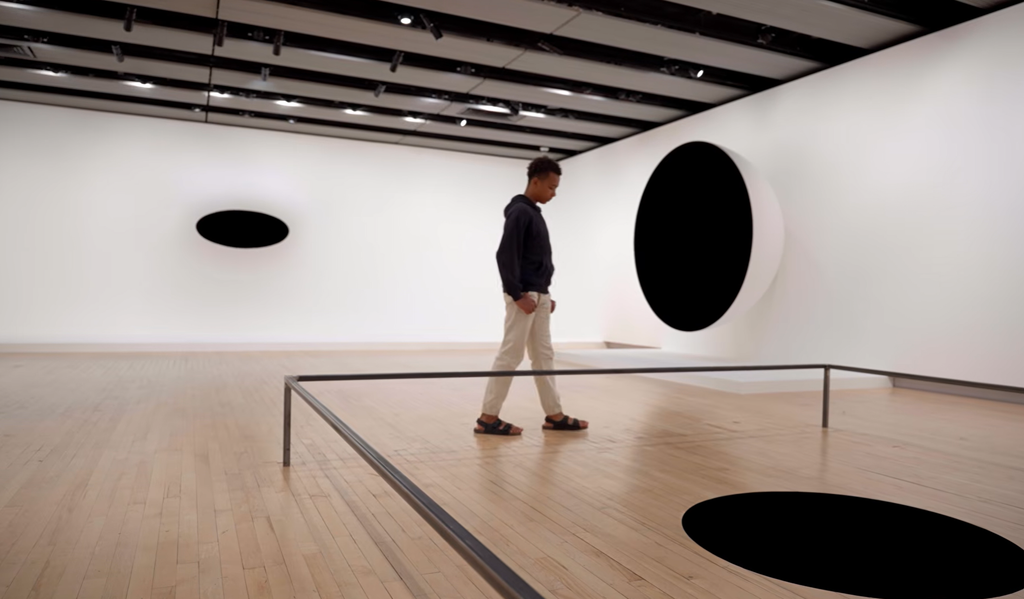 A gallery visitor looking at Kapoor’s round and oval sculptures, their solid black centres creating the illusion of endless, deep voids.