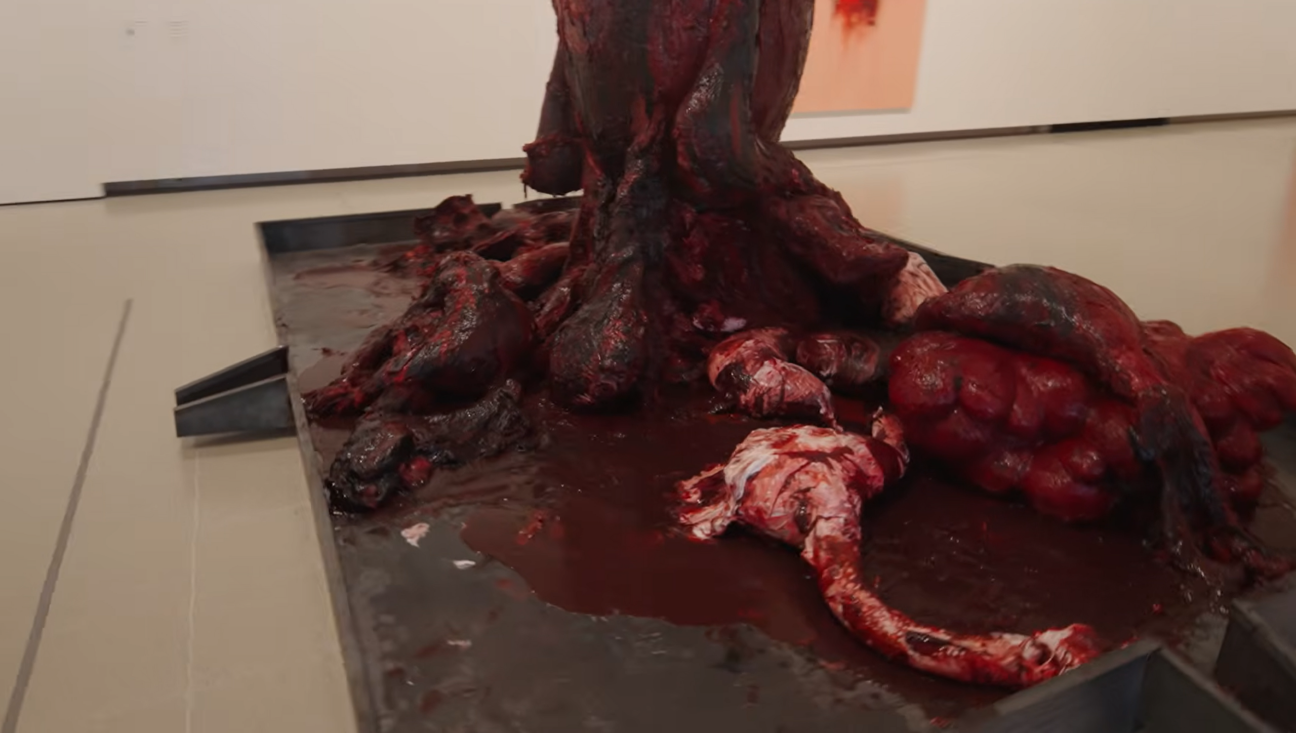 Close-up of a contemporary art installation featuring simulated red, fleshy remains dripping into industrial trays.